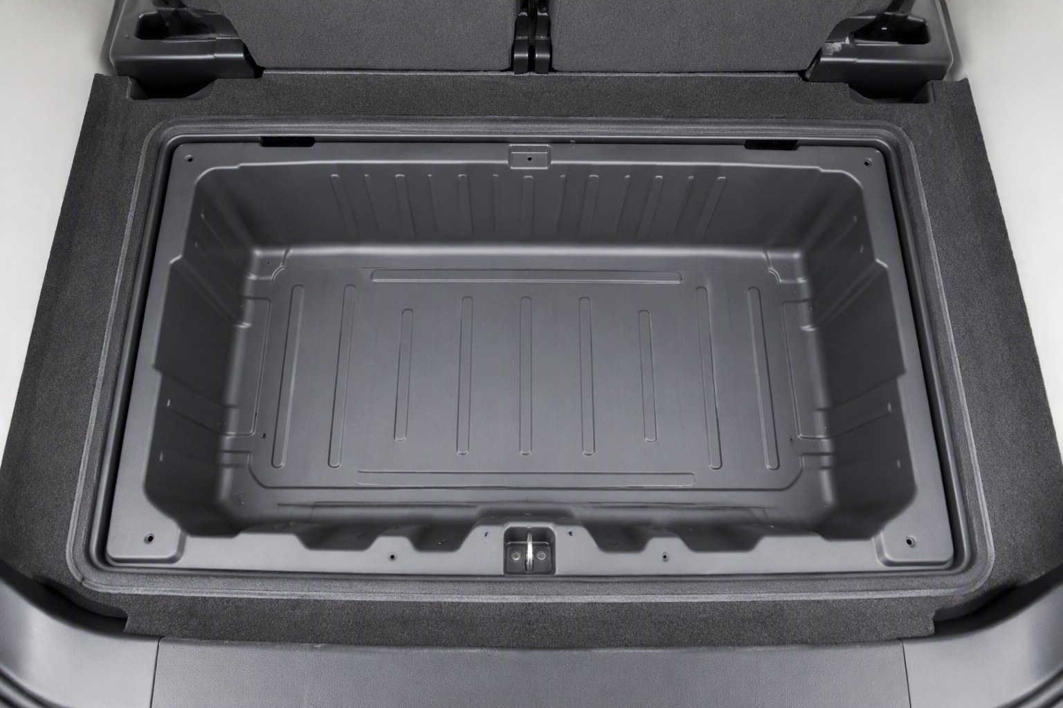 Top-down view into an open in-floor storage compartment showing pressed sheet metal recessed into the floor pan